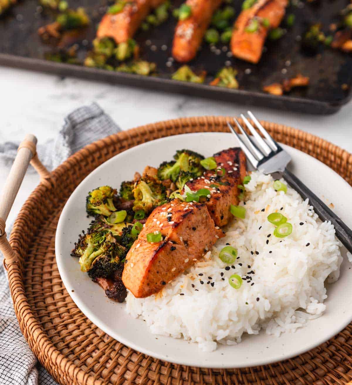 baked fillets on a plate with rice and broccoli with pan and more salmon in background
