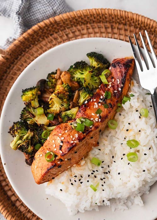 spicy korean salmon topped with green onion and sesame seeds on a plate next to rice and veggies