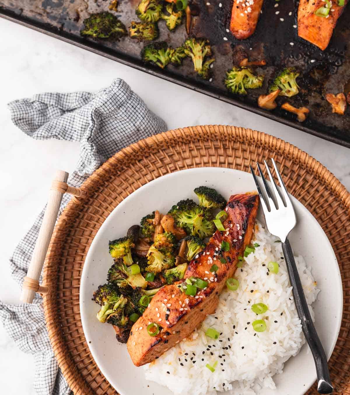 Asian style salmon topped with green onion and sesame seeds on a plate next to rice and veggies