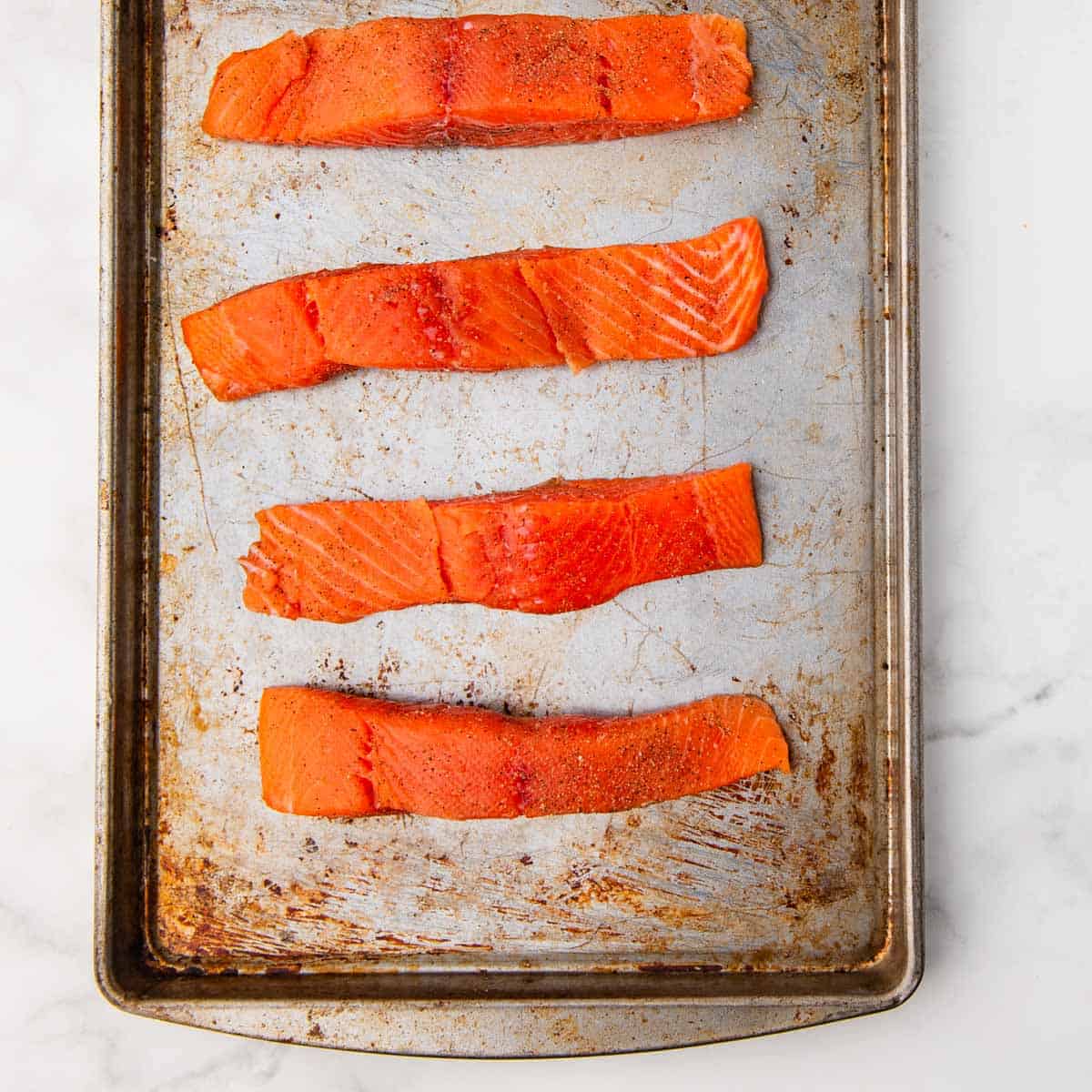 raw salmon fillets seasoned with salt and pepper on a baking sheet