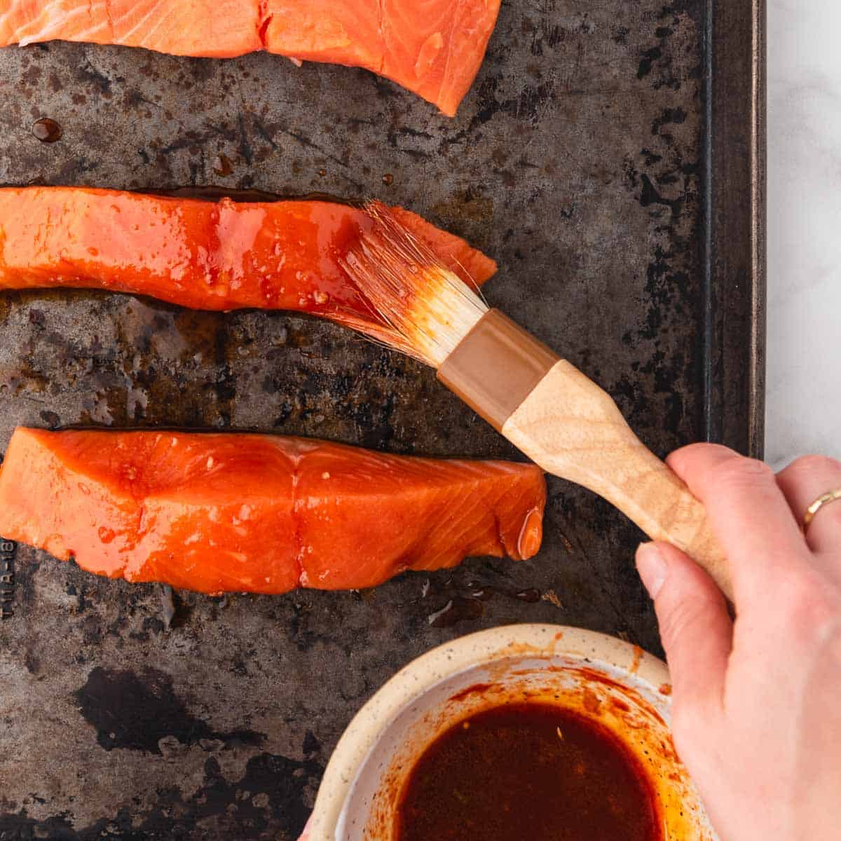hand brushing Korean sauce onto salmon fillets
