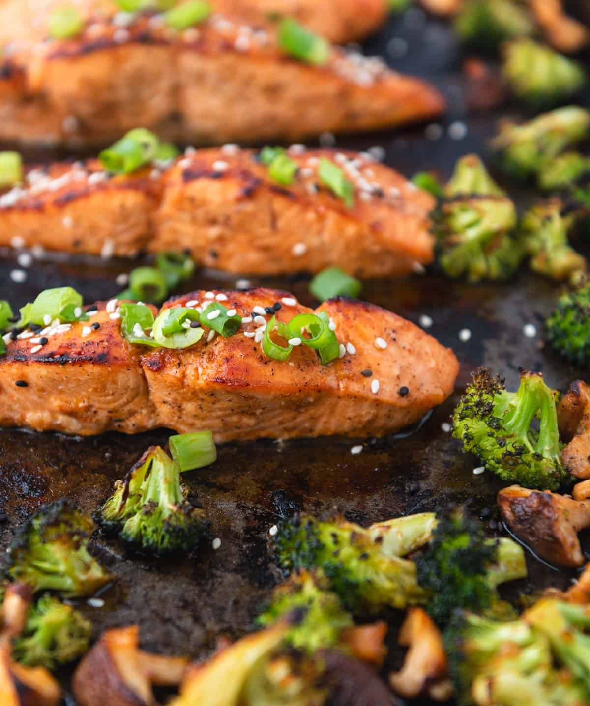 baked salmon filets with broccoli and mushrooms on a dark baking sheet