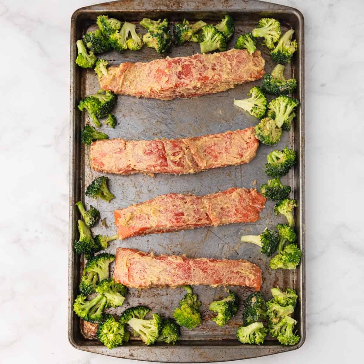 raw salmon topped with butter laid out on a baking sheet next to broccoli