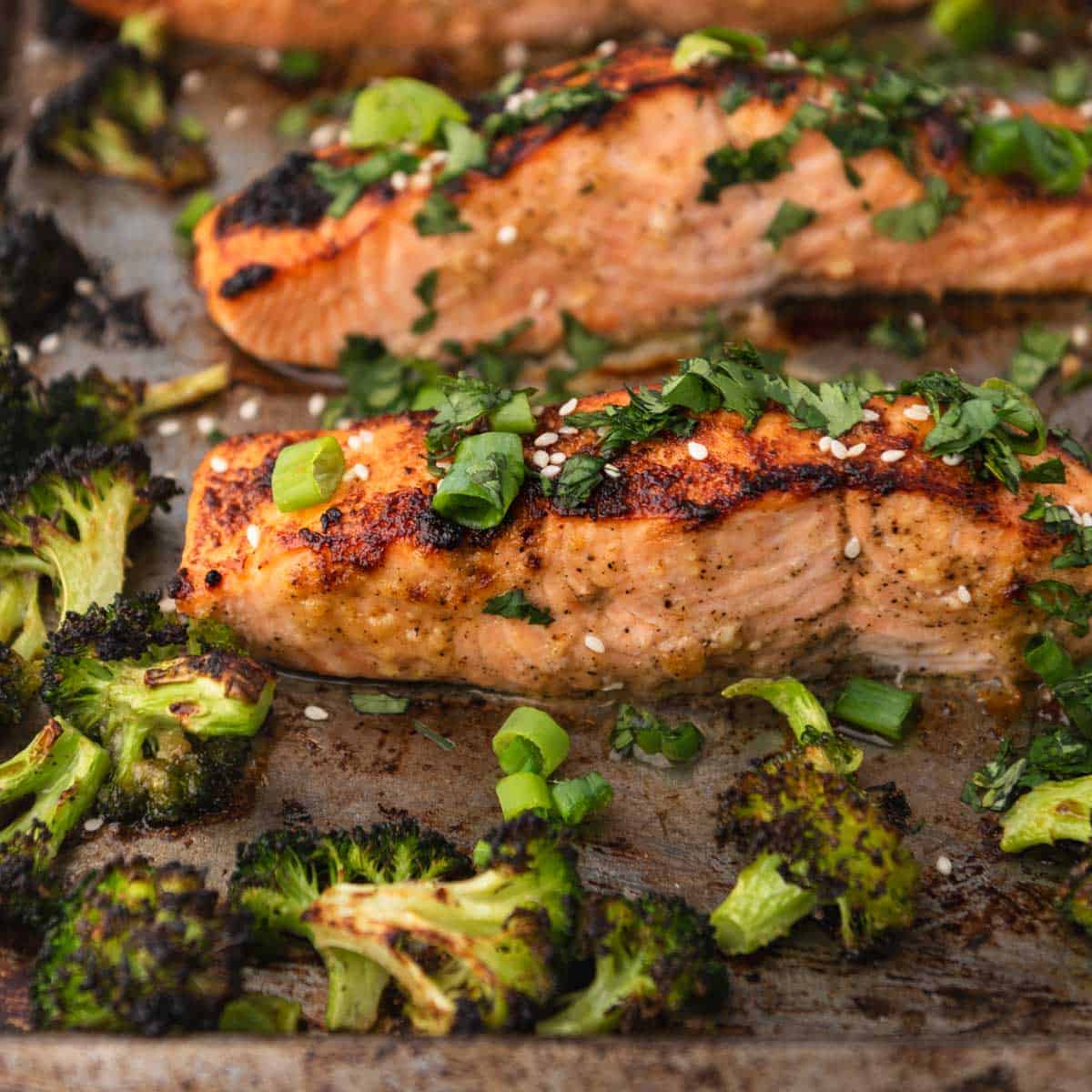 close up of Miso butter salmon topped with cilantro, green onion and sesame seeds next to broccoli on a sheet pan