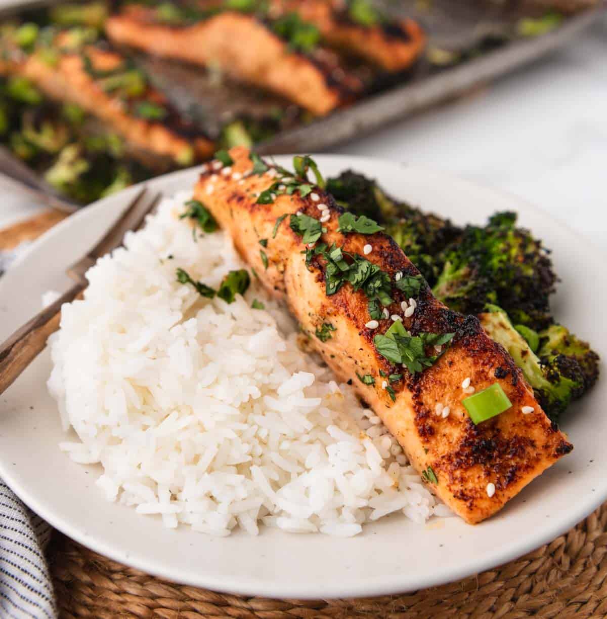 Miso butter salmon close up topped with cilantro, green onion and sesame seeds next to broccoli and rice on a plate