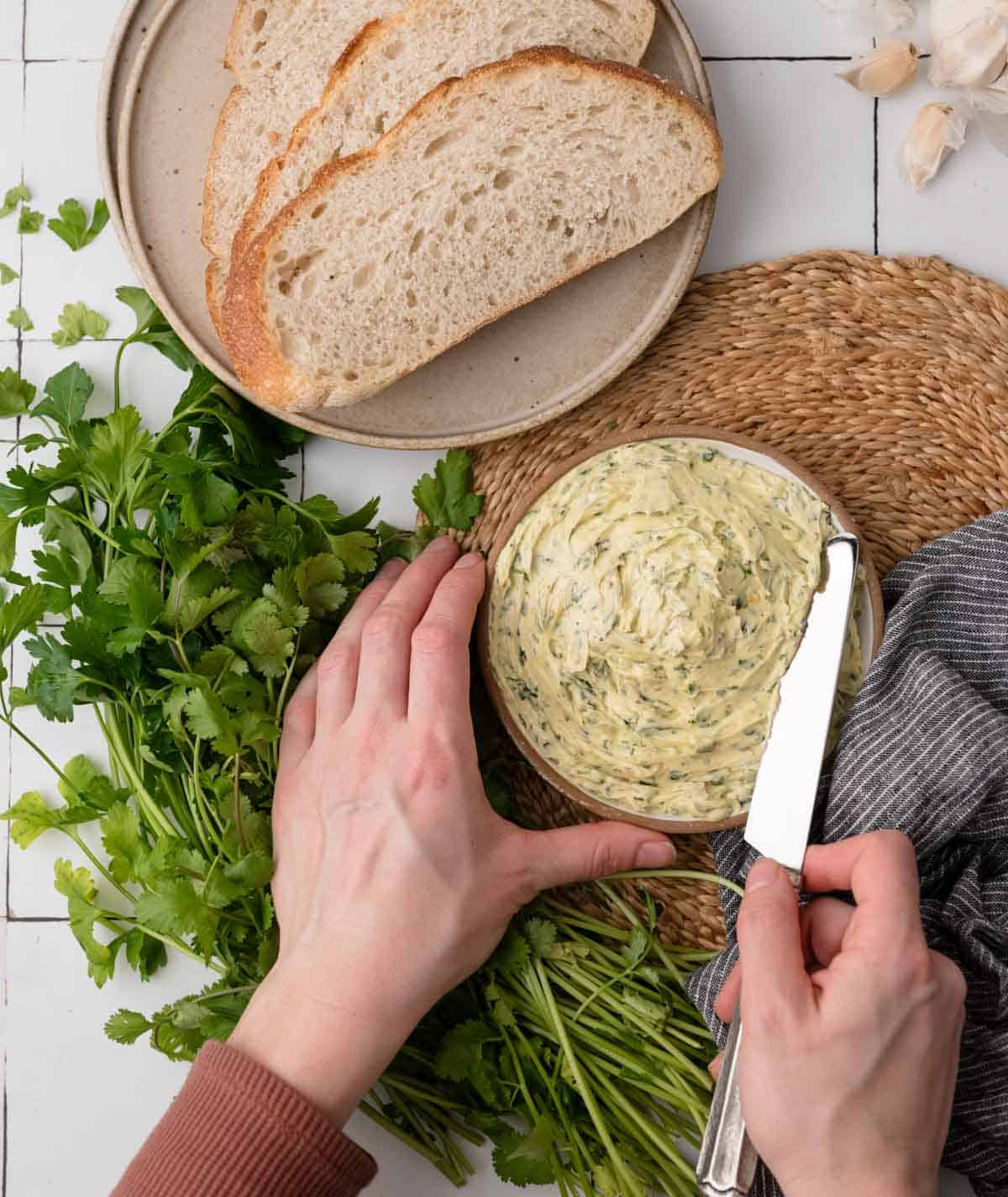 herb butter in a dish with hands holding it and a knife cutting into it