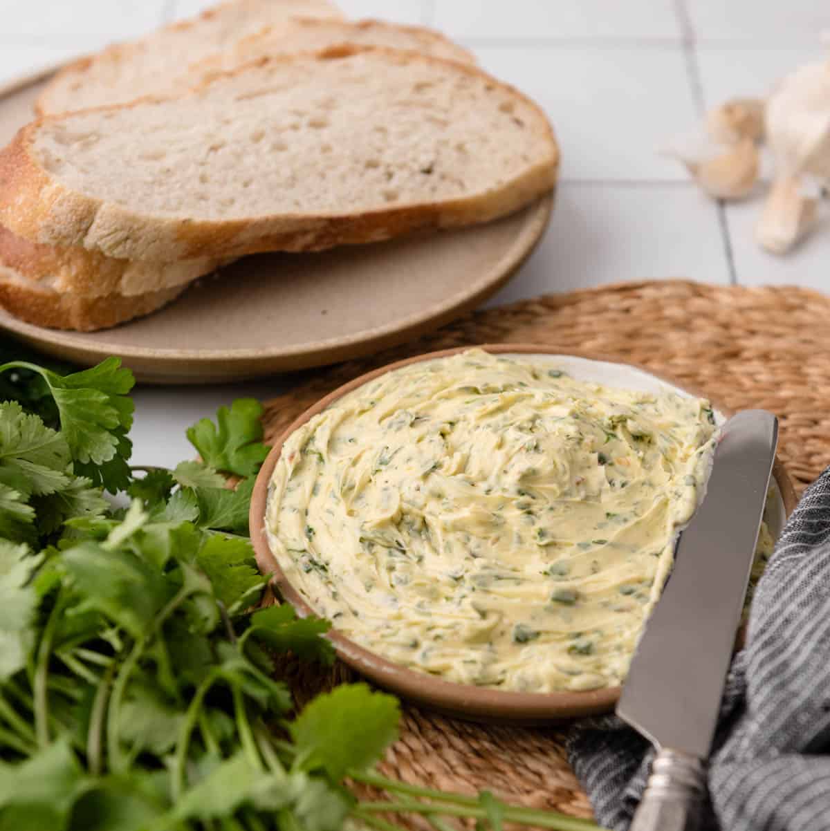 chimichurri butter on a plate with a knife, bread, parsley and cilantro next to it