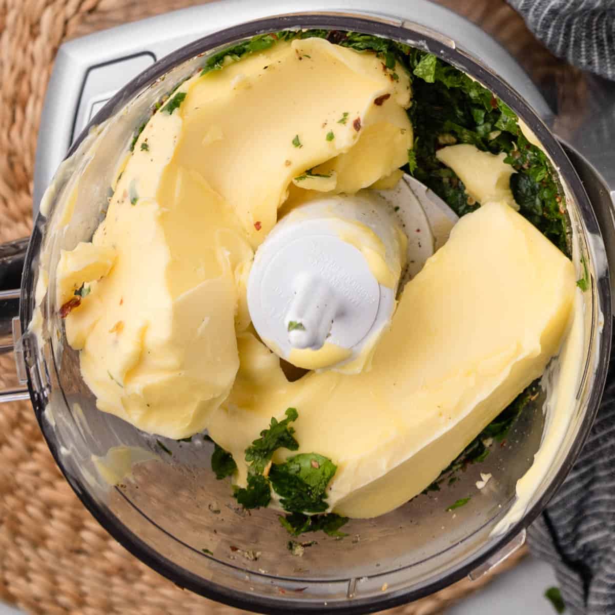 two sticks of soft butter on top of blended herbs in a food processor