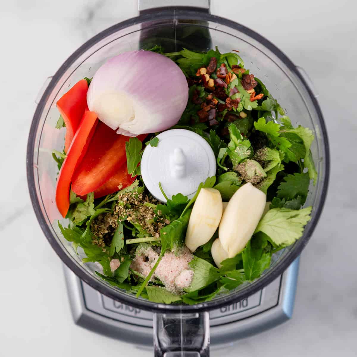 food processor with cilantro and other herbs, seasonings, garlic, shallot and red pepper in it