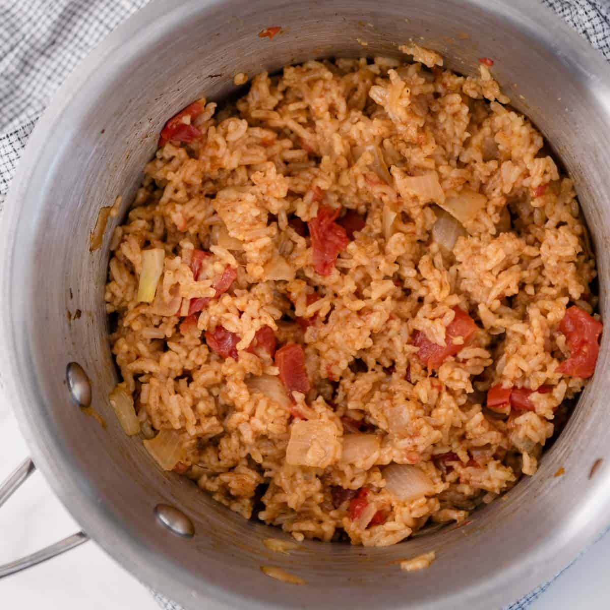 rice in a pot with cooked tomatoes and onions in it