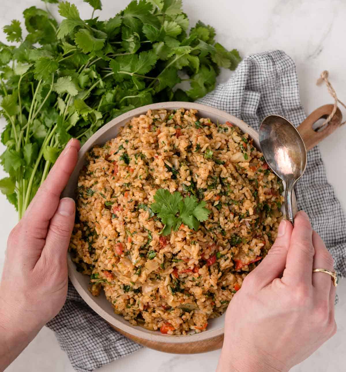Hands holding bowl of herb tomato rice about to dig into it with a spoon