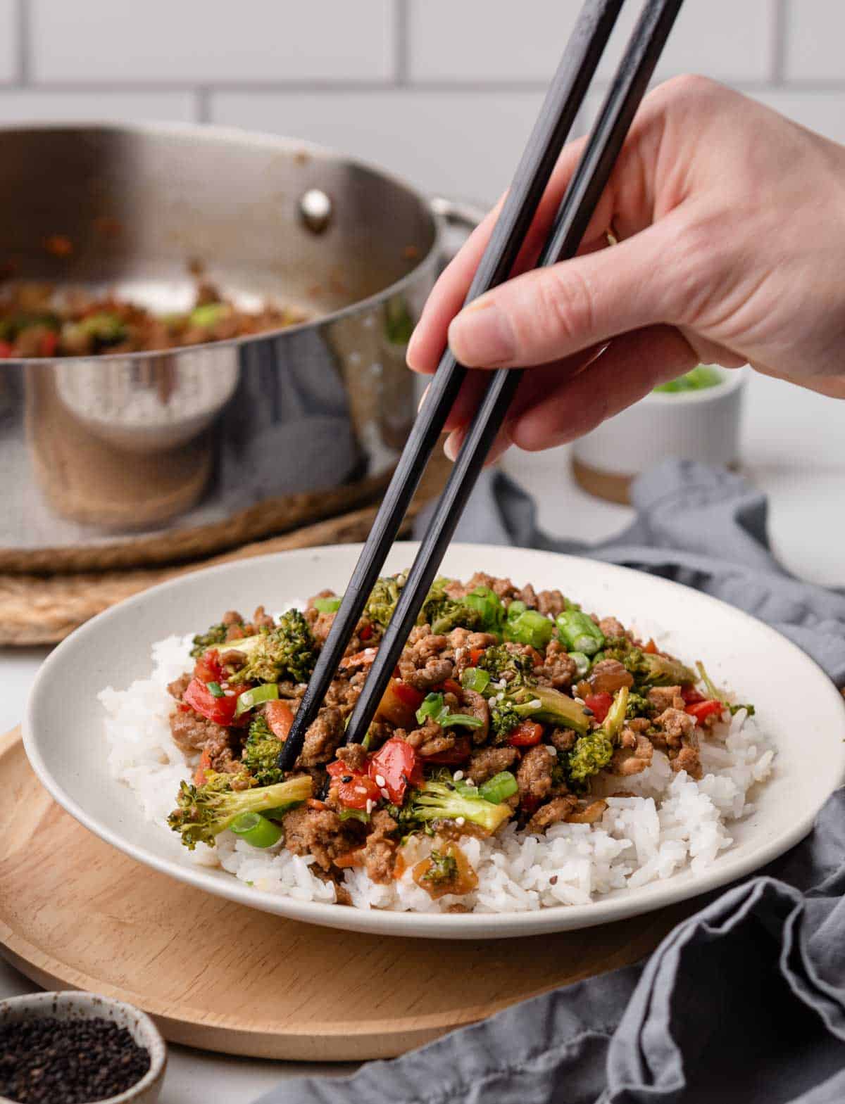 Hand using chopsticks to get a bite of stir fry from a plate