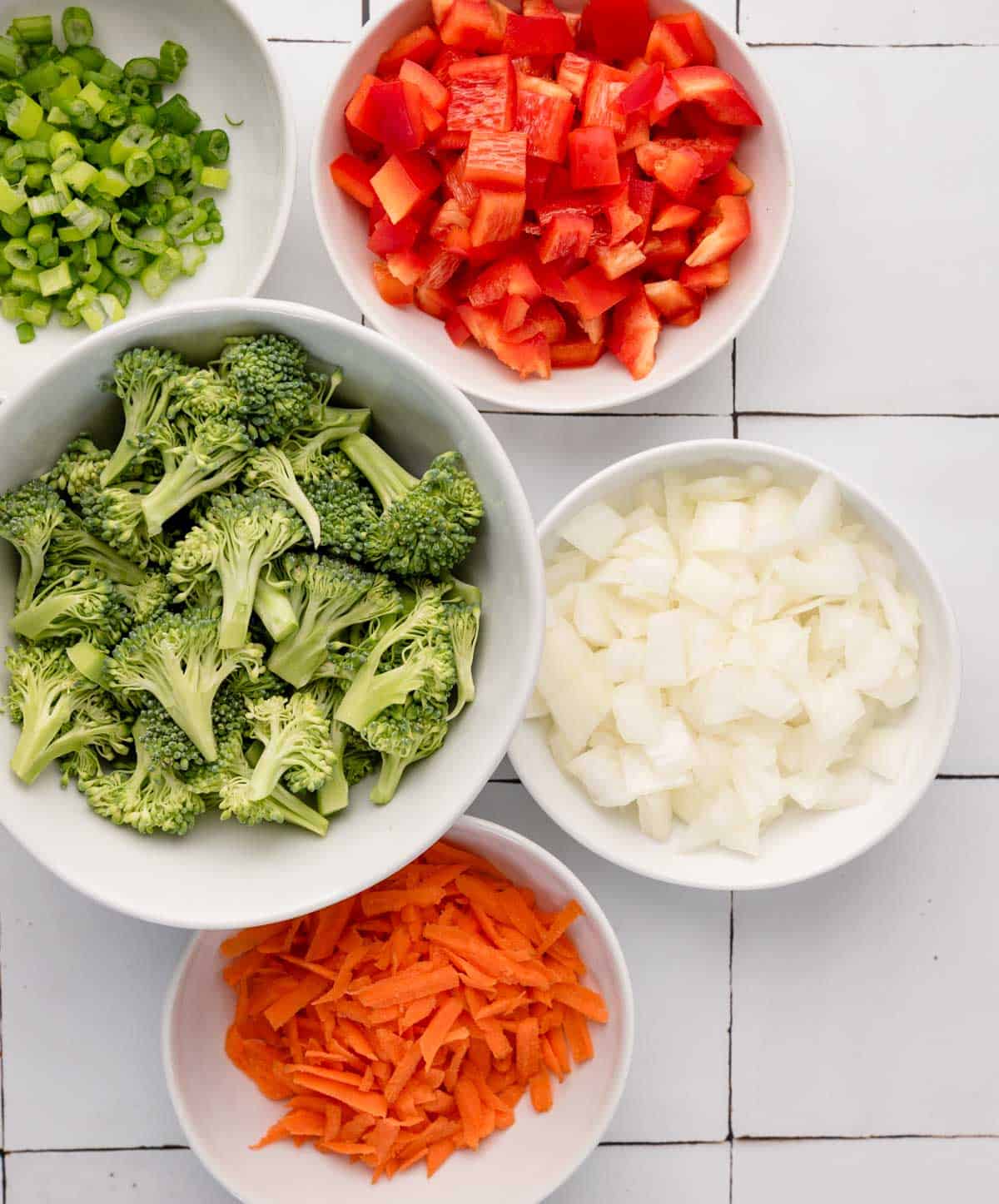 chopped vegetables (carrot, peppers, onion, green onion and broccoli) in white bowls from overhead