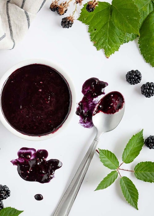 balsamic blackberry vinaigrette in a white small bowl next to blackberry leaves and branches