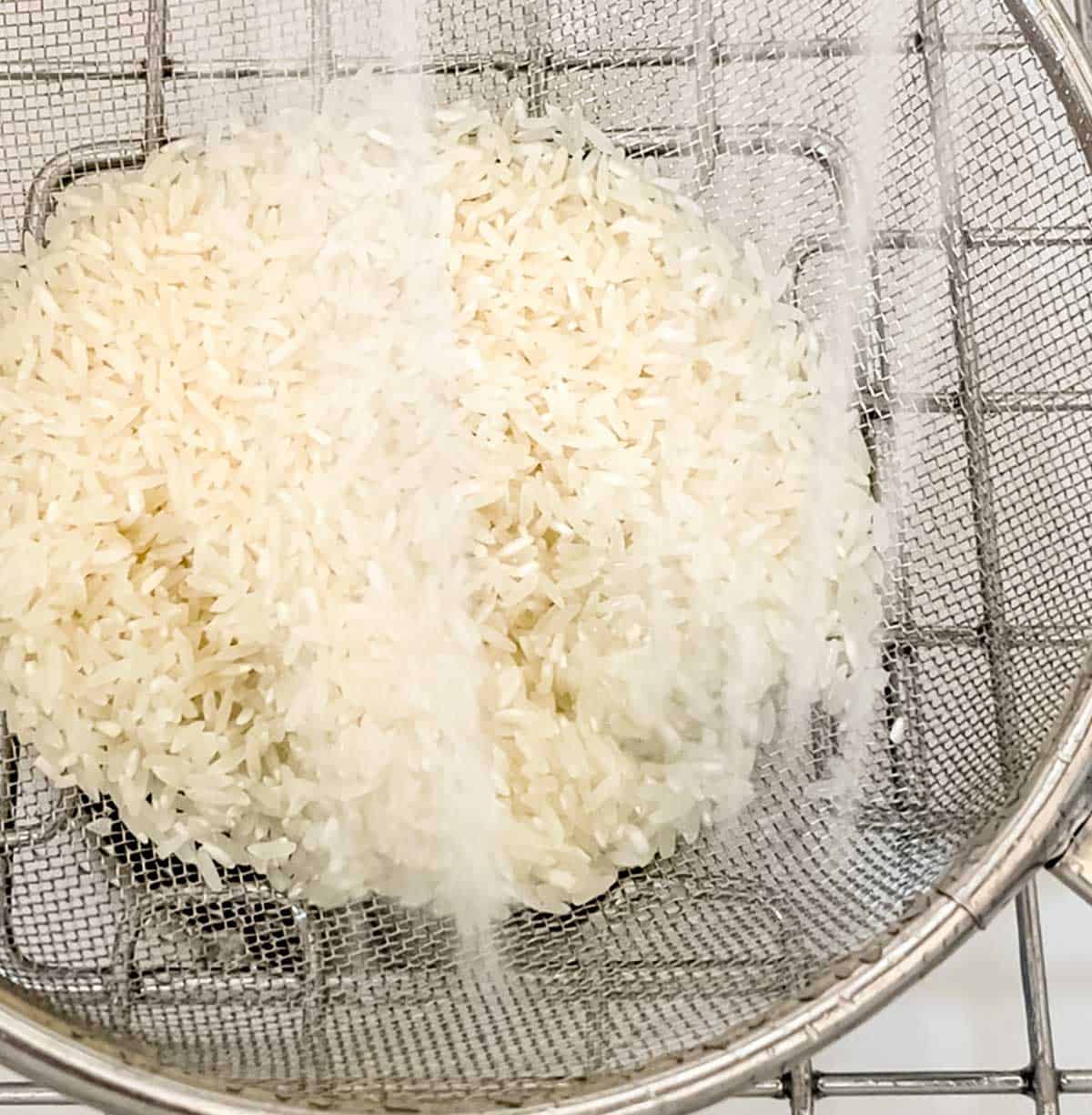 Rice in a mesh strainer being rinsed in the sink