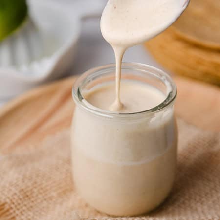 spoon drizzling creamy fish taco sauce into a glass jar