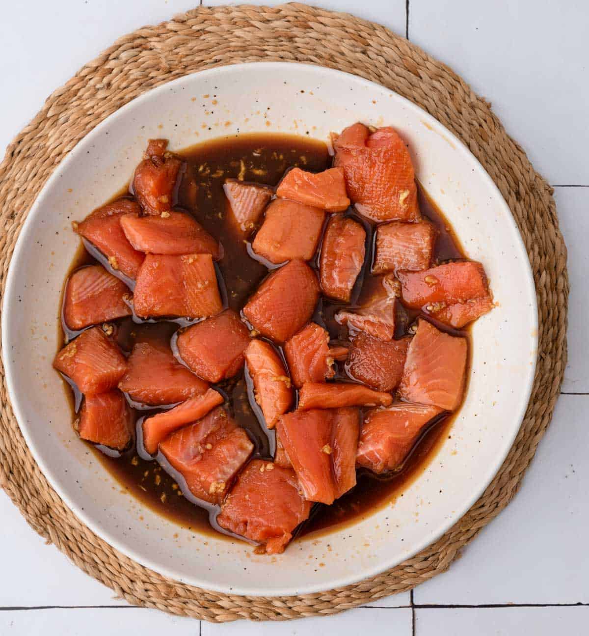 squares of salmon in a white bowl of dark teriyaki sauce