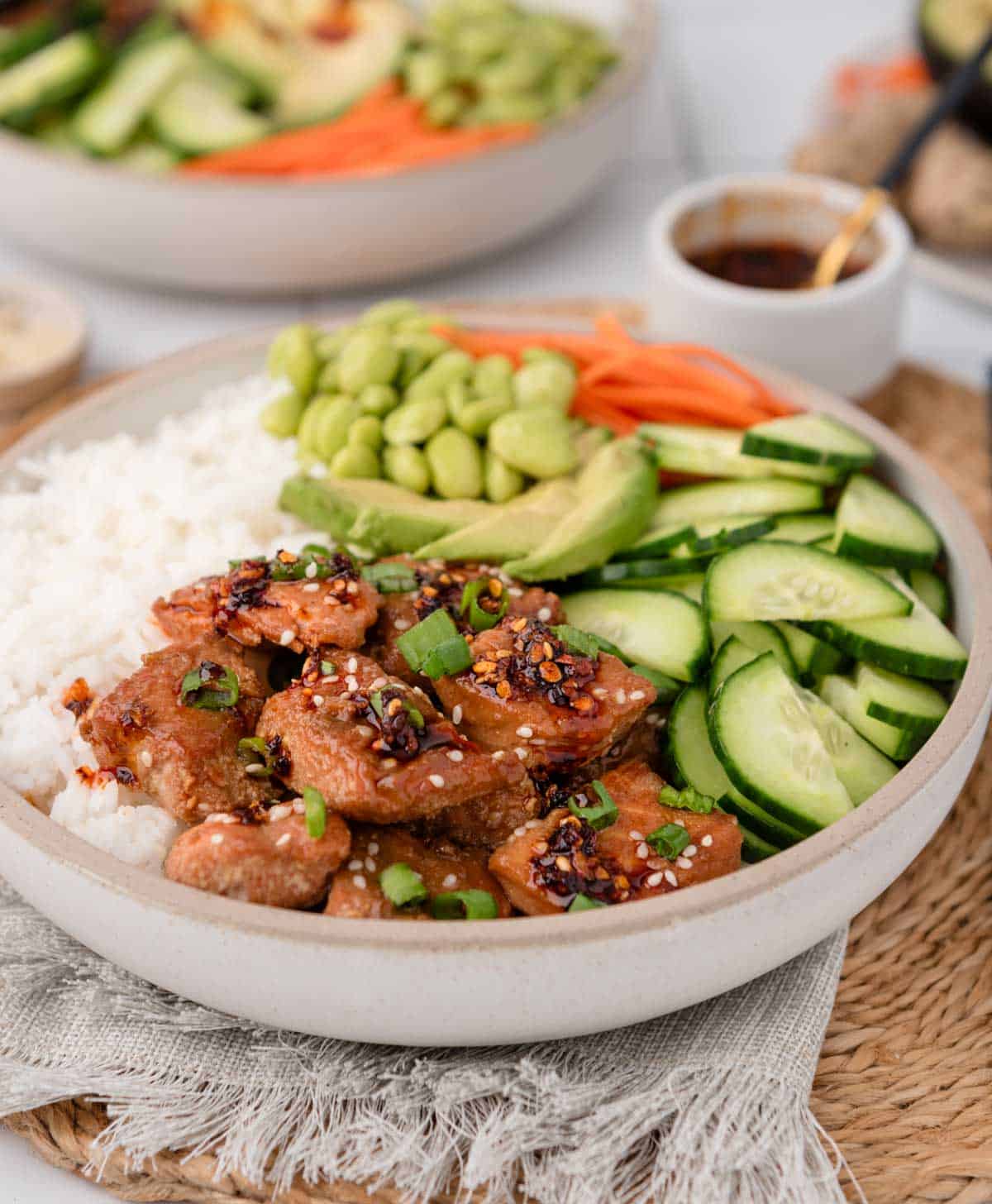 Side angle of cooked salmon bites on top of rice with cucumber and other veggies on it
