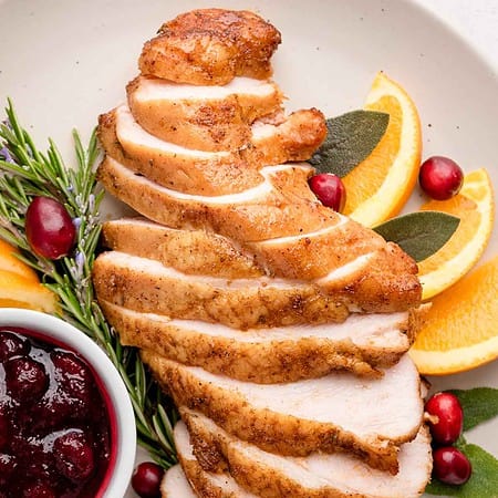 close up of plated sliced smoked turkey breast next to a bowl of cranberry sauce and garnishes