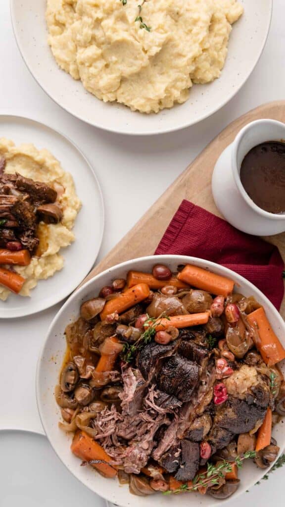 Cranberry pot roast next to mashed potatoes and gravy on a white table