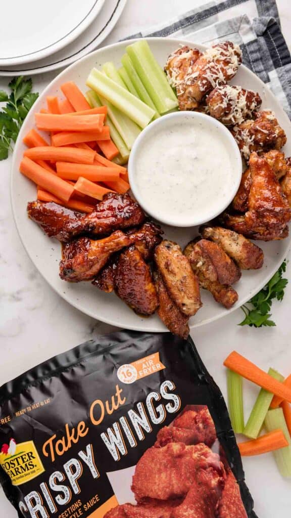 Product photo with bag of crispy wing packaging next to platter of cooked chicken wings with ranch, carrots and celery sticks