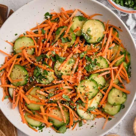 A bowl of cucumber carrot salad topped with chopped cilantro and sesame seeds.