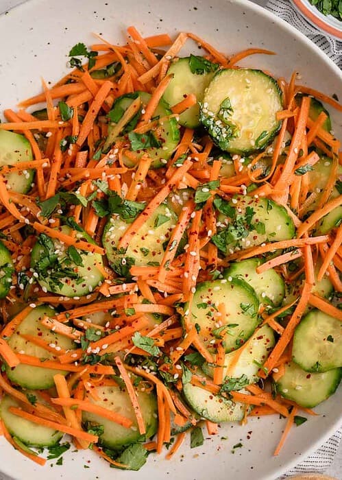 A bowl of cucumber carrot salad topped with chopped cilantro and sesame seeds.