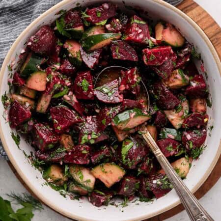 A bowl of beet and cucumber salad with herbs, mixed with a spoon.