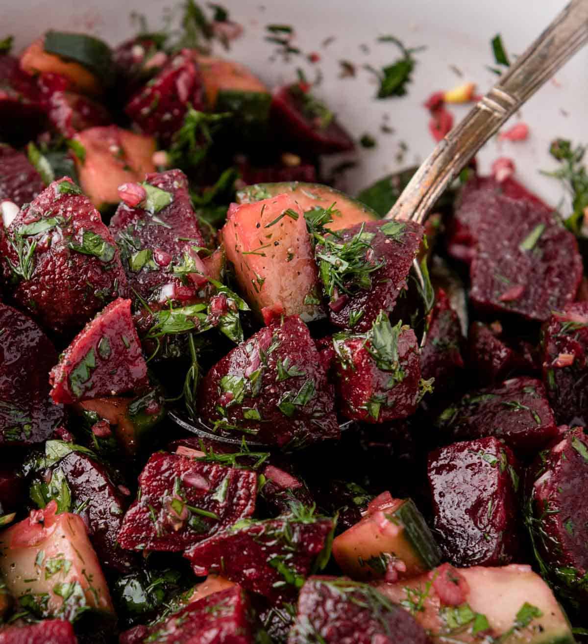 Close-up of a beet and cucumber salad with chopped herbs, mixed with a spoon.