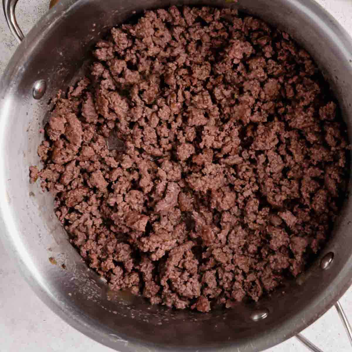 Cooked ground beef in a large stainless steel pot, viewed from above.