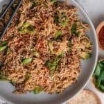 Mongolian Ground Beef Noodles with broccoli, green onions, sesame seeds, and red pepper flakes on a plate with chopsticks.