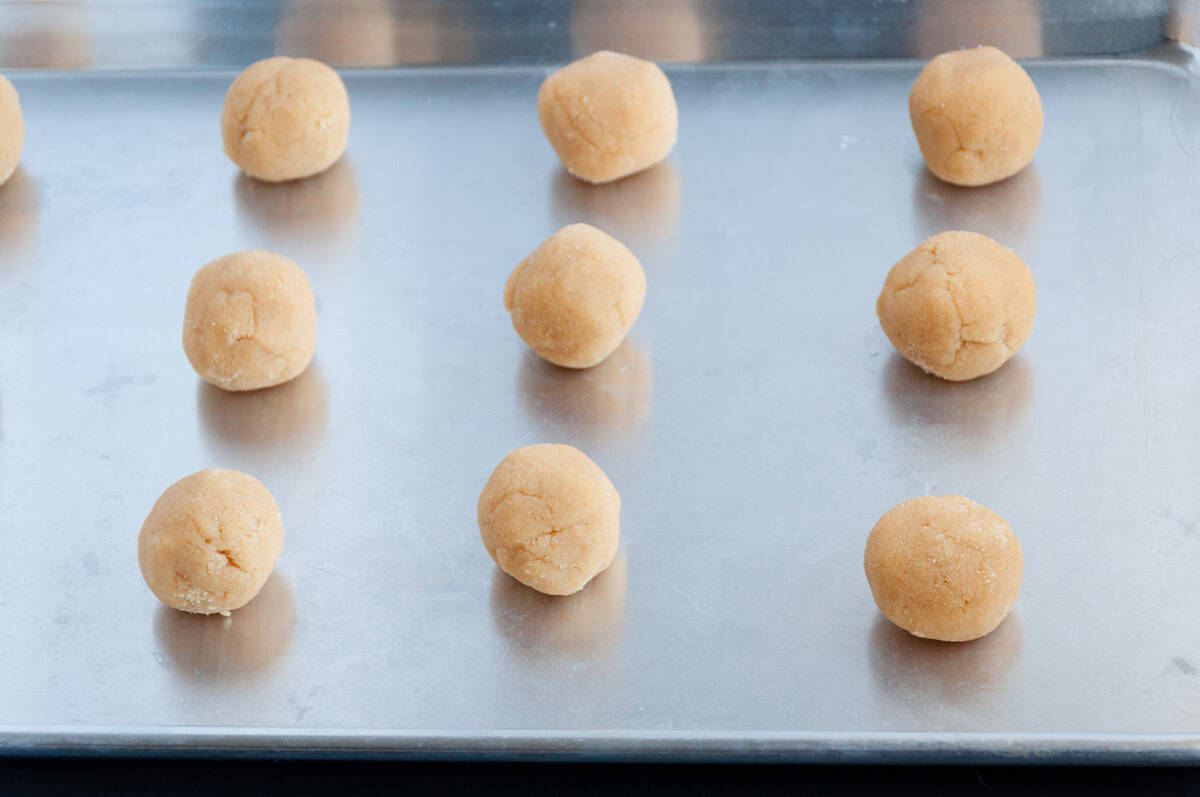 Balls of raw cookie dough are evenly spaced on a metal baking sheet.