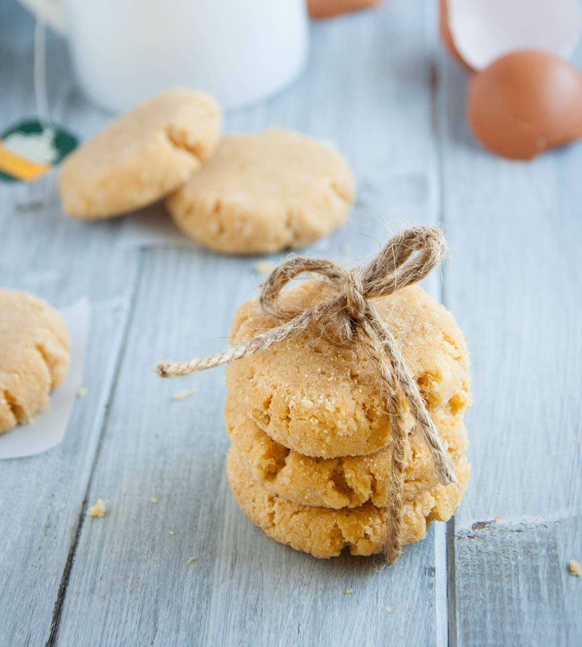 Three cookies tied with twine, stacked on a wooden surface, with more cookies and egg shells in the background.