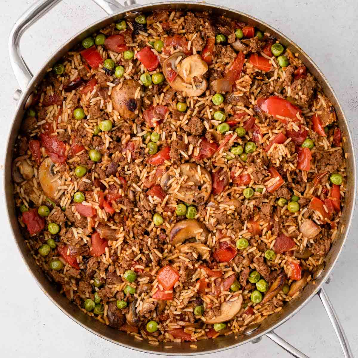 A pan filled with rice, ground meat, peas, mushrooms, tomatoes, and red bell peppers.