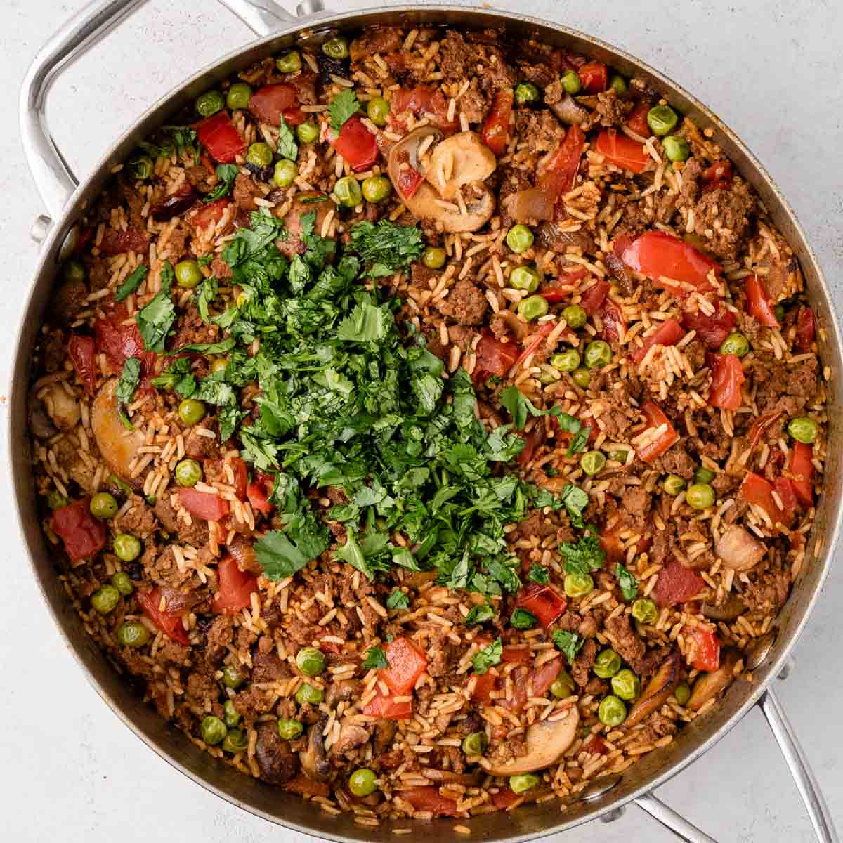 A skillet of rice with peas, red peppers, mushrooms, and topped with fresh chopped cilantro.