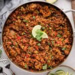 A skillet of chorizo rice garnished with lime wedges and cilantro on a light surface.