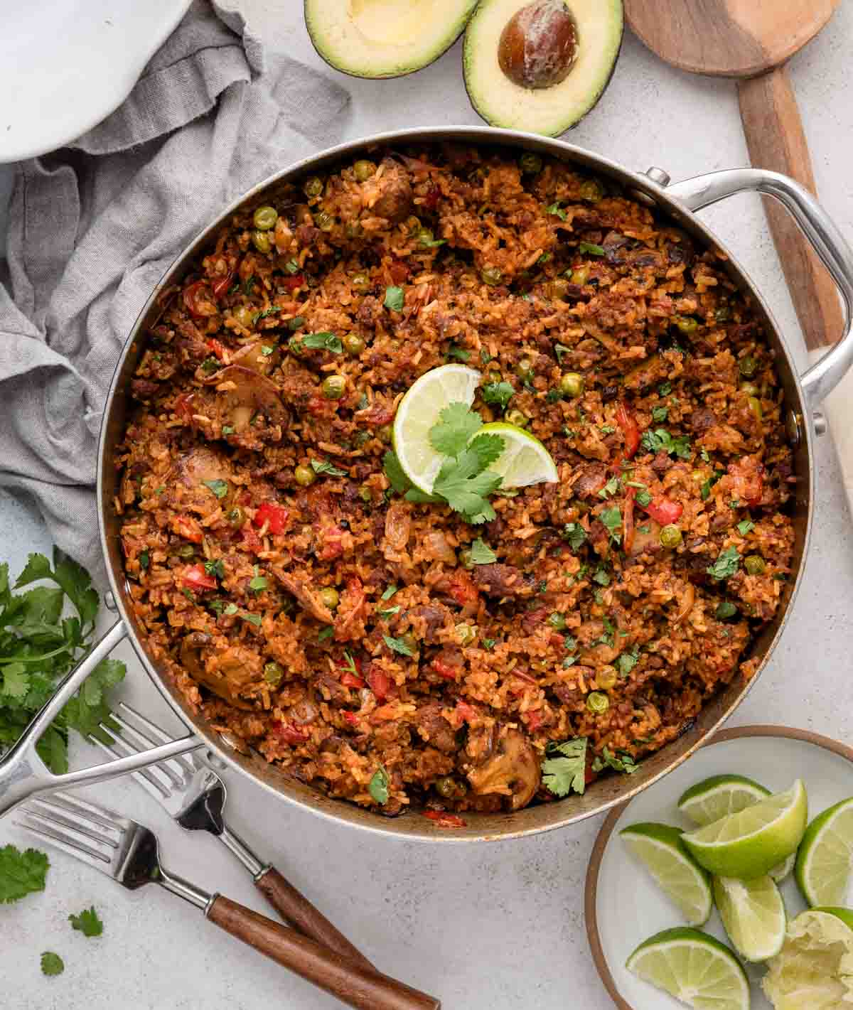 A large pan of chorizo rice garnished with lime and cilantro, surrounded by lime wedges and avocado.