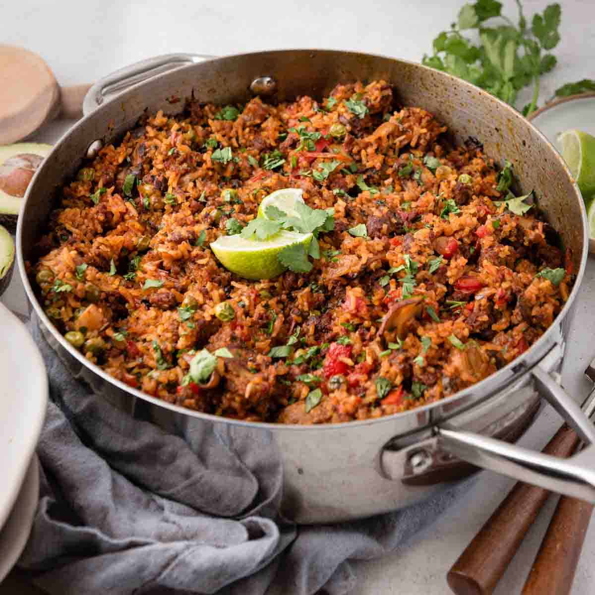 A large pan filled with flavorful, colorful chorizo rice and vegetables, garnished with fresh herbs and lime wedges.