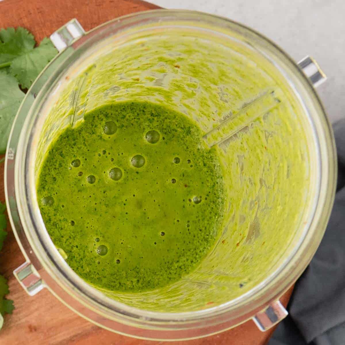 A blender cup filled with bright green smoothie, viewed from above, on a wooden surface.