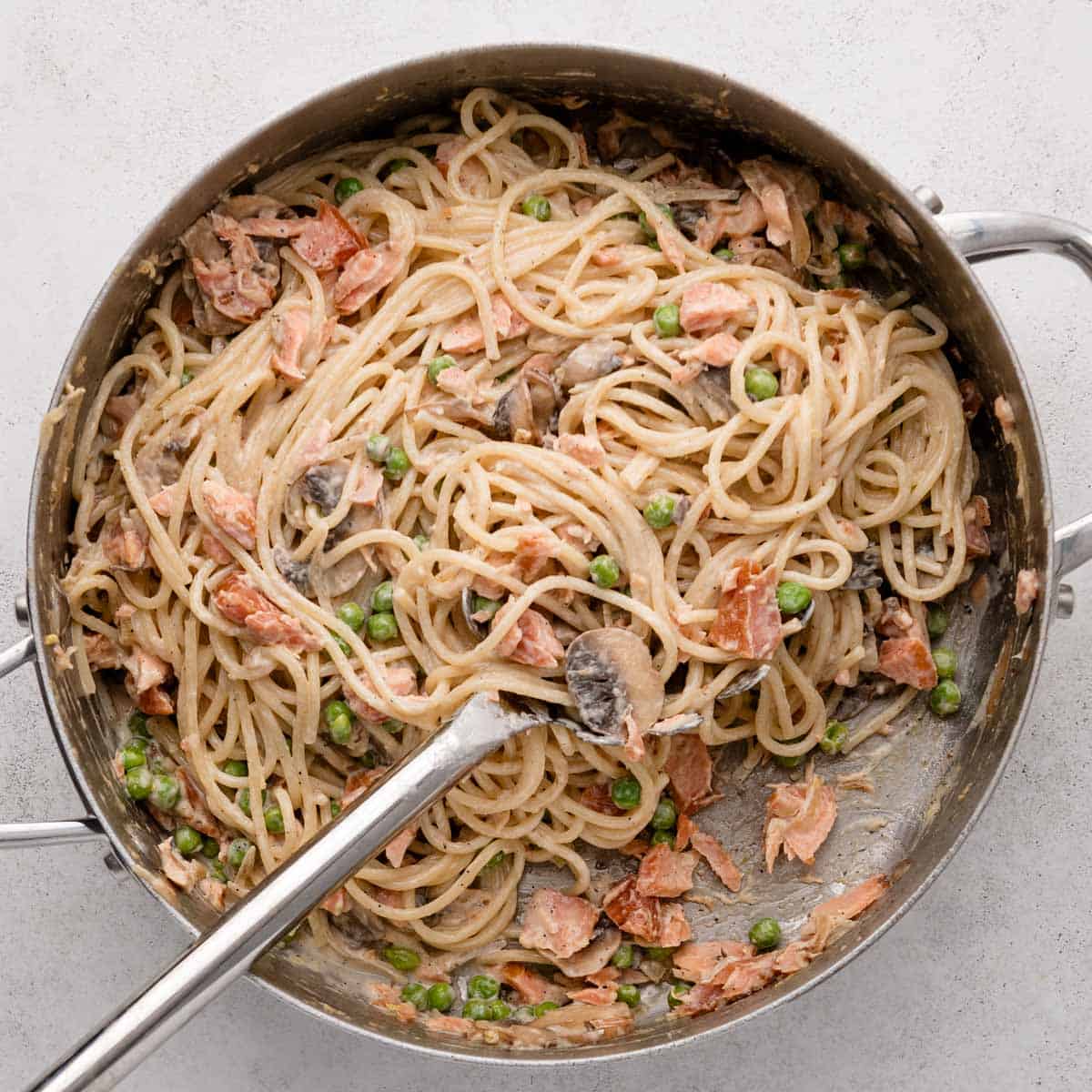 Spaghetti with peas, mushrooms, and pieces of bacon or ham in a creamy sauce in a large metal pan.