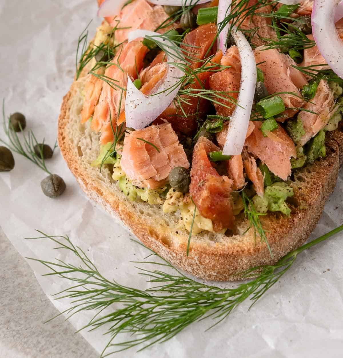 Open-faced sandwich with smoked salmon, red onion, capers, dill, and avocado on rustic bread.