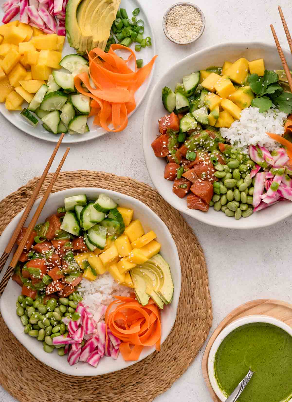 Two colorful salmon poke bowls with diced fish, mango, cucumber, edamame, carrot ribbons, rice, and avocado.