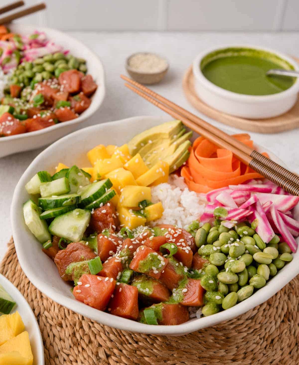 A colorful salmon poke bowl with rice, diced fish, mango, avocado, cucumber, edamame, radish, and sesame seeds.