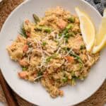 A plate of salmon and asparagus risotto, topped with grated cheese and served with lemon wedges.