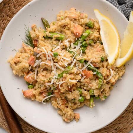 A plate of salmon and asparagus risotto, topped with grated cheese and served with lemon wedges.