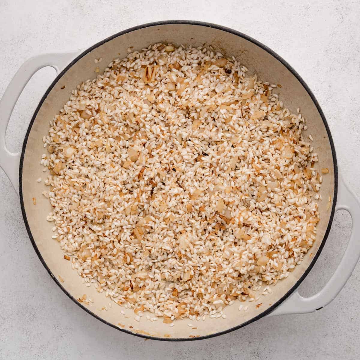 A pot filled with sautéed rice and onions, lightly browned, on a light-colored surface.