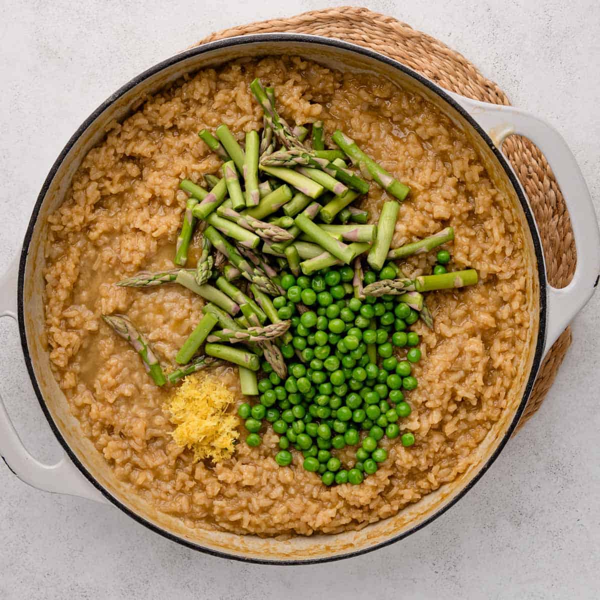 A pot of risotto topped with fresh asparagus, green peas, and a small pile of lemon zest.
