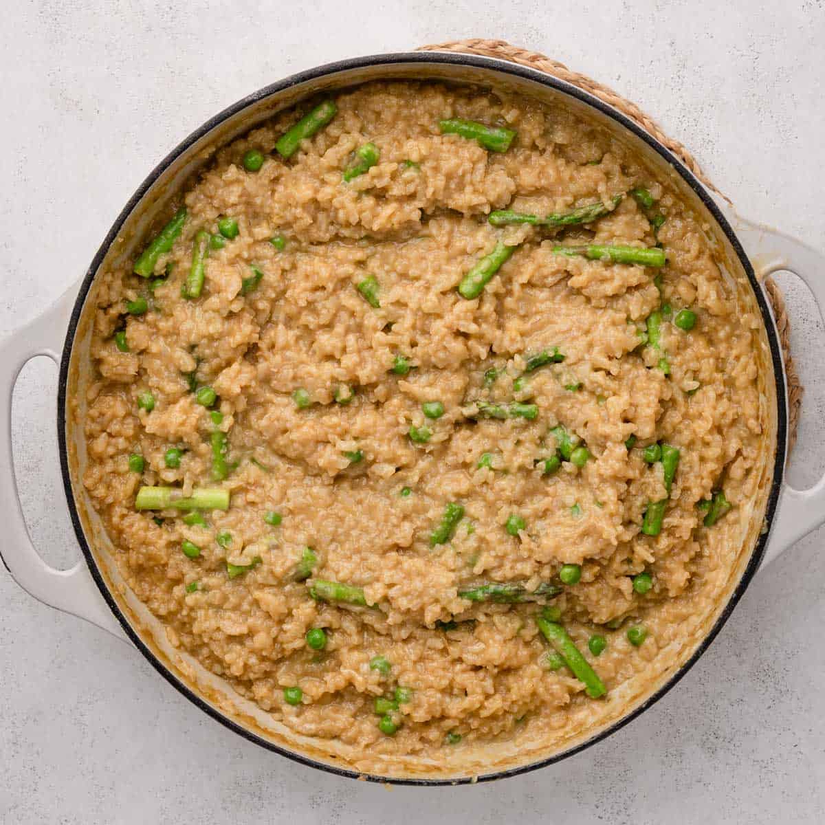 Creamy risotto with green asparagus and peas in a round white pot on a light background.