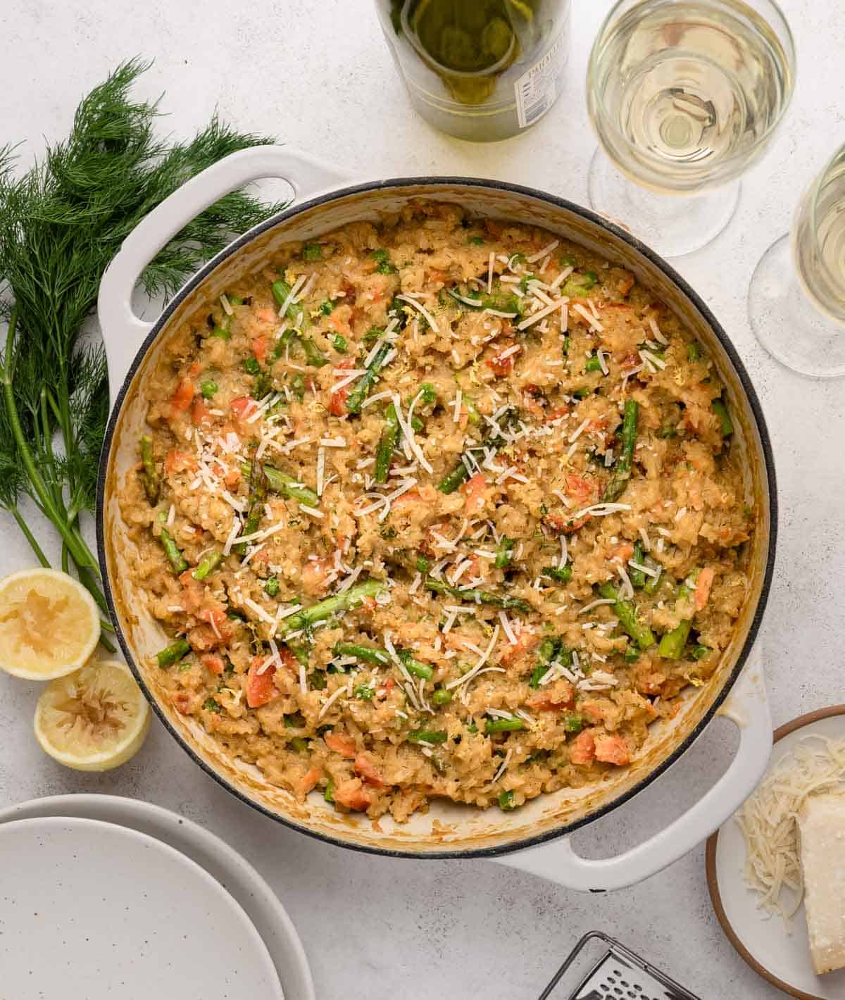 Creamy smoked salmon risotto in a white pot, garnished with herbs and cheese, next to glasses of white wine.