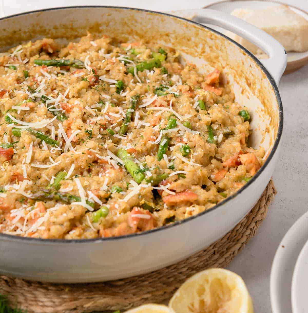 A pan of smoked salmon risotto topped with grated cheese, with lemon halves and cheese in the background.